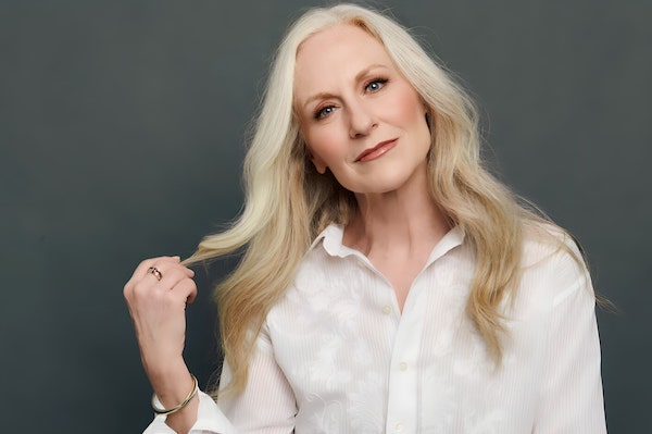 Elizabeth Ward Land in white shirt twirling hair against dark grey backdrop.